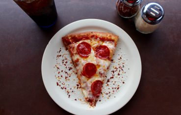 pepperoni pizza slice on a plate with red pepper flakes